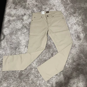 LEE byxor - Snygga beige byxor från Lee, modell Daren Zip Fly Regular Straight. Klassisk femficksdesign, rak passform och dragkedjegylf. Tillverkade i mjuk bomull med en stilren look som passar till det mesta. Perfekta för dig som gillar enkel och clean stil.