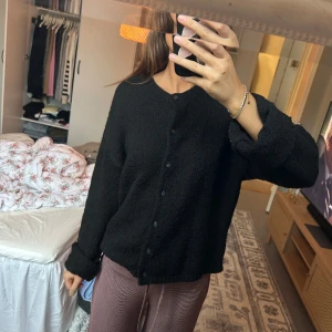 Svart stickad kofta med knappar - Mysig svart stickad kofta med rund hals och knäppning framtill. Koftan har en enkel och clean look med långa ärmar och en lite loose passform. Perfekt att slänga på sig när det är kyligt ute.