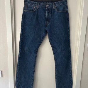 Levi's 501 blå jeans W33 L34 - Klassiska Levi's 501 jeans i mörkblå denim. Rak passform med fem fickor, knappgylf och ikonisk läderpatch bak i midjan. Perfekta för dig som gillar tidlös stil och vill ha ett par jeans som funkar till allt.