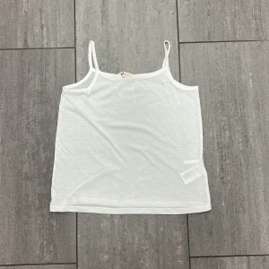 Vit linnetopp från H&M - Enkel och stilren vit linnetopp från H&M med tunna axelband. Toppen är rak i modellen och tillverkad i mjuk bomull, perfekt för varma dagar eller som lager under andra plagg. Passar dig som gillar en clean och basic look.