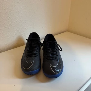 Nike Mercurial Zoom fotbollsskor svart/blå - Säljer ett par Nike Mercurial Zoom fotbollsskor i svart med blå detaljer och blå sula. Skorna har snörning, låg profil och är tillverkade i syntetmaterial. Perfekta för inomhusspel med sin greppvänliga sula och sportiga look.använda etc bar gånger men helt nya.
