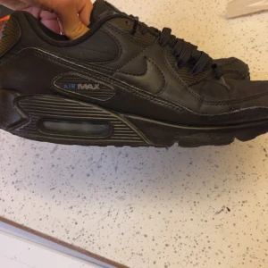 Svarta Nike Air Max sneakers - Säljer ett par helsvarta Nike Air Max sneakers med klassisk synlig luftbubbla i sulan. Skorna har en mix av skinn och textil, rund tå och snörning. Perfekta för dig som gillar en clean och sportig look.
