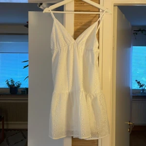 Vit sommarklänning från SHEIN - Superfin vit kortklänning från SHEIN med smala axelband och v-ringning. Klänningen har broderade blommor i tyget och volang nertill för en söt och luftig känsla. Perfekt för varma dagar och har en lätt, flowy passform.
