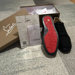 Christian Louboutin - Exklusiva svarta sneakers från Christian Louboutin i mocka med ikonisk röd sula och broderad logga på hälen. Skorna har snörning och en stilren, rund tå. Insidan är fodrad i ljust skinn för extra komfort. Perfekta för dig som vill sticka ut med lyxig streetstyle.