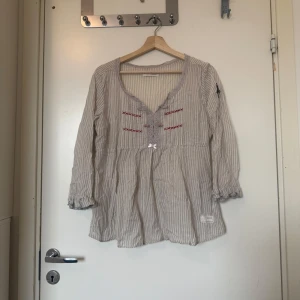 Odd molly blus  - Säljer en otroligt vacker blus som är i en creme färgad bottenfärg men gråa ränder. Den har ett fint odd molly märke på ena armen. Samt broderi och spetsdetaljer vid bysten. Från märket Odd Molly i storlek 3 som enligt deras storleksguide motsvarar en storlek M/L. Mycket fint skick, jag hittar inga synlig anmärkningar eller defekter. 