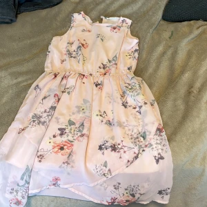 Ljusrosa blommig klänning Kappahl 146 - Superfin ljusrosa klänning från Kappahl i storlek 146. Klänningen är ärmlös med ett vackert blommigt mönster och har en lätt, luftig känsla. Perfekt för sommarens alla tillfällen med sin flowiga kjol och feminina look.