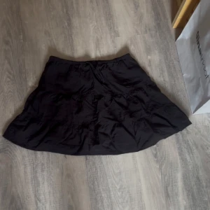 Svart kortkjol från Divided XS - Svart kortkjol från Divided i storlek XS. Kjolen har en lätt utställd form och resår i midjan för skön passform. Tillverkad i tunn bomull, perfekt för varma dagar. Enkel och stilren design som är lätt att matcha med olika toppar.