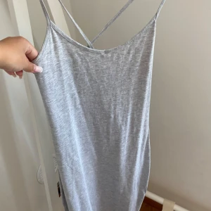 Grå sommarklänning från New Yorker - Ljusgrå, enkel och stilren klänning från  New Yorker med smala axelband som korsas i ryggen. Klänningen är ärmlös och har en rak, tight passform i mjuk bomull. Perfekt för varma dagar när du vill ha något bekvämt och snyggt.