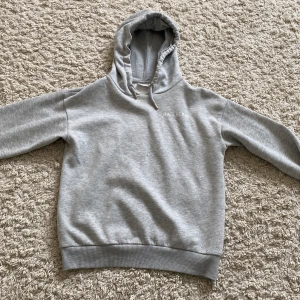 Grå hoodie Ma Chérie Gina Tricot - Grå hoodie från Gina Tricot med trycket 'Ma Chérie' och två hjärtan på ryggen. Tröjan har huva med snörning och ribbade muddar vid ärmslut och nederkant. Perfekt för en chill och avslappnad stil.