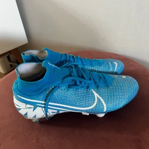 Nike Mercurial Superfly  - Säljer ett par Nike Mercurial Superfly 360 fotbollsskor i blått med vita detaljer och text. Skorna har snörning, högt skaft och metall-dobbar för bästa grepp på planen. Ovandelen är i stickad syntet för en tight passform och maximal bollkontroll. Påsen ingår även , passar även 42