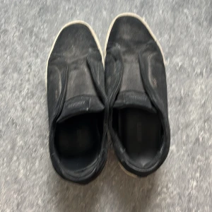 Arigatos - Svarta slip-on sneakers från Ahimsa med vit sula. Skorna har en minimalistisk design utan snörning och är tillverkade i textilmaterial. Perfekta för en avslappnad och stilren look.