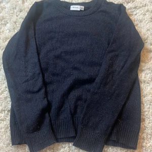 Mörkblå stickad tröja från Vila - En klassisk mörkblå stickad tröja från Vila i storlek XS. Tröjan har rund halsringning, ribbade muddar vid ärmslut och nederkant samt lång ärm. Perfekt för lager-på-lager och enkel att matcha med jeans eller kjol. 