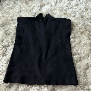 Svart ärmlös polotröja med half zip - Svart ärmlös polotröja med ribbad hög krage och en snygg half zip-dragkedja baktill. Tröjan är stickad och har en clean, minimalistisk look som passar perfekt till lager-på-lager. Den har även axelvaddar! I strl S från Vero Moda och är som ny🥰