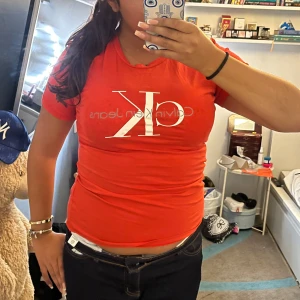 Röd Calvin Klein t-shirt - Snygg röd t-shirt från Calvin Klein med stor vit CK-logga framtill. Modellen är figurnära med korta ärmar och rund halsringning. Perfekt för dig som gillar klassiska logotyper och enkel stil. Materialet känns mjukt och skönt mot huden.