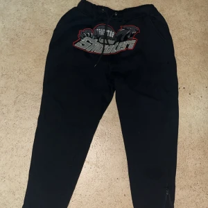 Svarta Trapstar byxor - Svarta mjukisbyxor från Trapstar med stort broderat shooters-tryck framtill. Byxorna har snörning i midjan, dragkedja vid benslut och en loose passform. Perfekta för chill eller streetwear-stil.