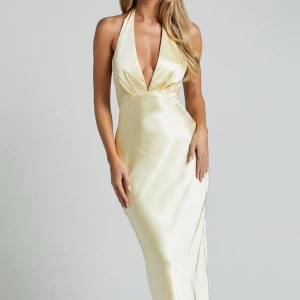 Ljusgul långklänning med halterneck och öppen rygg - Säljer en helt oanvänd klänning. Den svarta rosetten medföljer ej. Nypris ca 1100kr. 