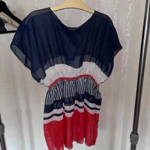 Randig blus i blått, vitt och rött - Snygg blus med  ränder i marinblått, vitt och rött. Blusen har resår i midjan, lös passform och korta ärmar. Materialet är tunt och luftigt, perfekt för varma dagar. 
