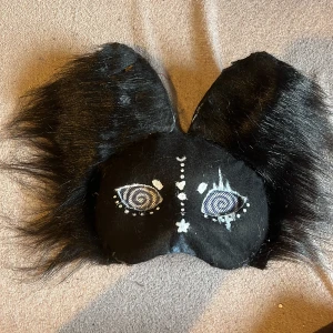 Therian mask kanin/katt - Handmade mask som är helt vegan och man ser bra i den, Unik svart mask med stora fluffiga öron och handmålade ögon med spiral-mönster. Masken har pälsimitation och elastiskt band för att sitta på plats.  Om du undrar över något kontakta mig! Och om du vill att jag ändrar något när du köpt den eller vill prata om priset säg bara till!!