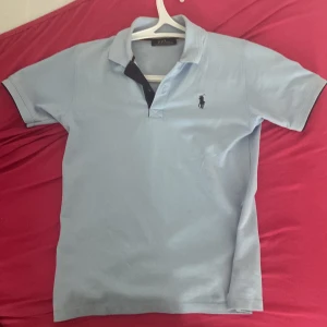 Ljusblå Polo Ralph Lauren t-shirt - Snygg ljusblå t-shirt från Polo Ralph Lauren med klassisk pikékrage och broderad logga på bröstet. T-shirten är kortärmad och tillverkad i bomull, perfekt för en clean och stilren look.