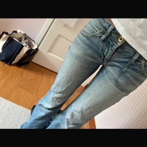 Blå bootcut jeans från Mexx - Snygga ljusblå jeans från Mexx med bootcut passform och klassisk femficksdesign. Jeansen har låg midja, slitningar och detaljer i guld på knappen. Perfekta för en avslappnad och trendig look.