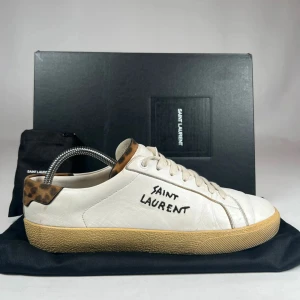 Saint Laurent skor - Lyxiga och snygga skor i vitt läder med cool leopardtouch. Bekväma, unika och passar både till vardag och annat. Använda men i fint skick! Strolek 40 men passar även 41. Original box samt med dust bag och extra laces följer med i köpet. 