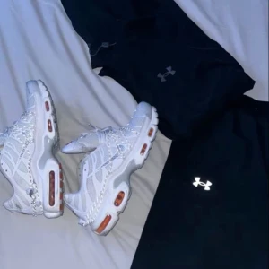 Nike TN Utility - Nike Air Max Plus sneakers i vitt med orange detaljer och synliga Air Max-bubblor i sulan. Skorna har mesh- och syntetmaterial, silverfärgad swoosh och snörning. Den sportiga designen och de unika linjerna gör dem till ett statement för dig som gillar streetwear.