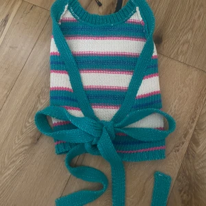 Randig stickad omlottopp från Zara - Superfin och eftertraktad stickad omlottopp från Zara i turkos, vitt och rosa med breda ränder. Toppen har knytband i midjan och är ärmlös med en öppen rygg. Perfekt sommar och strandtopp. Den är helt oanvänd och enbart testad.