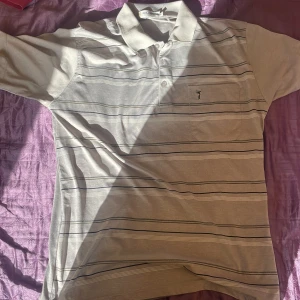 Randig grå pikétröja från Goldmen - Snygg grå pikétröja från Goldmen med tunna svarta och vita ränder. Klassisk krage, knäppning med två knappar och en bröstficka med broderad logga. Perfekt för en chill och stilren look. Tillverkad i mjuk bomull som känns skön mot huden.