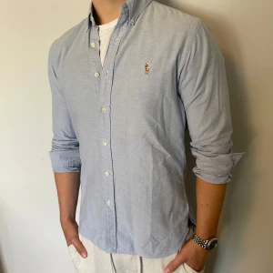 Ralph lauren skjorta - Säljer denna riktigt snygga ljusblåa Ralph lauren skjorta, den är i mycket bra skick utan några defekter, storlek M modell slim fit, den är 76 cm lång och 50 cm bred under armhålorna, hör gärna av dig vid frågor!