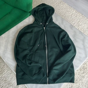 Mörkgrön hoodie med dragkedja från H&M - Mörkgrön hoodie från H&M med hel dragkedja framtill och justerbar huva med snören. Tröjan har långa ärmar, ribbade muddar och två fickor på sidorna. Skick 10/10 inga defekter alls storlek S.