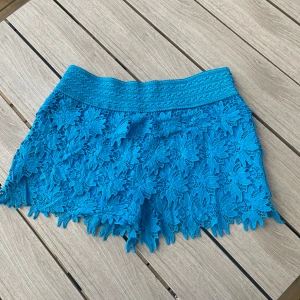 Turkosa spets-shorts från Ella S/M - Superfina turkosa shorts från Ella i storlek S/M. De har ett brett, elastiskt midjeband och är täckta av detaljerad blommig spets med snyggt mönstrad kant. 