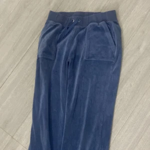 Blå mjukisbyxor i frotté med snörning - Mysiga blå mjukisbyxor i frotté med bred resår och snörning i midjan. Stora fickor fram och bak, bakfickan har lock med knappar. Perfekta för chill eller häng hemma.