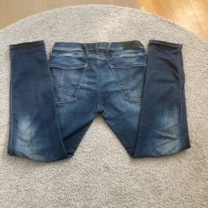 Blå Replay jeans, storlek 31/32 - Säljer ett par snygga blå jeans från Replay i storlek 31/32. Jeansen har klassisk femficksdesign, snygga slitningar och kontrastsömmar på bakfickorna. De är tillverkade i mjukt denimtyg och har en normal passform med raka ben.