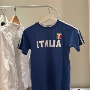 Blå Italien fotbollströja Boy Studio - Snygg blå fotbollströja från Boy Studio med texten ITALIA och Italiens flagga på bröstet. Egentligen en barnstorlek, jag har använt som baby tee.