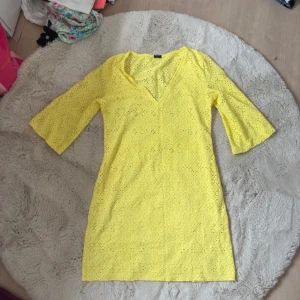 Strandklänning - Superfin gul kortklänning från Calzedonia med v-ringning och trekvartsärm. Klänningen har broderade cirkelmönster och är gjord i bomull, vilket gör den luftig och perfekt för varma dagar. Snygg och lekfull stil som verkligen sticker ut!