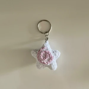 Virkad stjärnformad nyckelring - Söt handvirkad nyckelring i form av en vit stjärna med en rosa swirl detalj Perfekt att hänga på väskan eller använda till nycklarna för en gullig touch. Fler virkade produkter finns på min profil, kan även göra specialbeställningar🩷