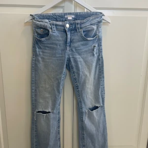 Ljusblå slitna jeans från Gina Tricot - Ljusblå jeans från Gina Tricot med slitningar och hål på knäna för en cool, avslappnad look. Klassisk femficksmodell med raka ben och snygga detaljer på bakfickorna. Perfekta för dig som gillar en trendig streetstyle. Dem har ett litet hål i bak vid fickan.