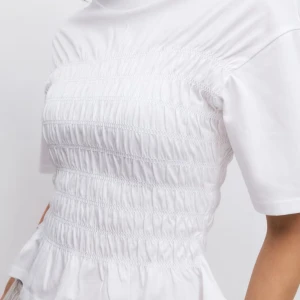 smockad topp  - Superfin vit topp med smockad front och korta ärmar från Gina Tricot. Modellen är croppad med rund halsringning och har en lätt volangkant nedtill. Perfekt för dig som gillar en söt och trendig stil.