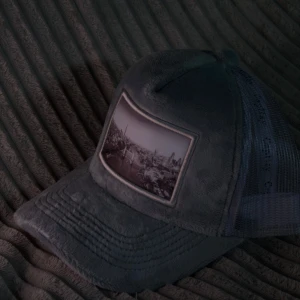 Grå velvetkeps  - Snygg grå keps från CapHay med mesh på sidorna och baksidan för extra ventilation. Framtill finns ett stort svartvitt fototryck av en stadsvy. Kepsen har böjd skärm och justerbar passform. Perfekt för dig som vill sticka ut med en unik accessoar. Har ungefär 70 stycken kvar så hör av er om ni vill köpa fler än en. Helt nya oanvända. Går att justera storleken på baksidan. Passar de flesta.