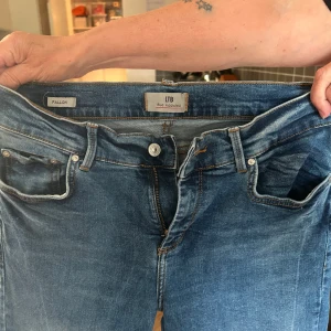 Blå bootcut jeans från LTB, W29 L32 - Snygga blå jeans från LTB i modellen Fallon. Jeansen har klassisk femficksdesign, bootcut-ben och normalhög midja. Tillverkade i mjukt denim med lätt slitningar och kontrastsömmar. Perfekta för dig som gillar en tidlös och avslappnad look. Passar någon som är runt 160 i längd. 