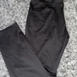 Svarta kostymbyxor från Blend - Svarta kostymbyxor från Blend med klassisk rak passform. Byxorna har fickor fram och hällor för bälte. Snygga och stilrena, perfekta till en dressad look. Materialet är mjukt och känns bekvämt mot huden.