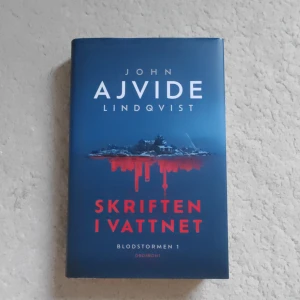 Skriften i vattnet - En spännande och modern kriminalroman av John Ajvide Lindqvist. Skriften i vattnet är första delen i trilogin Blodstormen och bjuder på en internationell thriller med oväntade vändningar, kärlek och mysterier. Perfekt för dig som gillar nervkittlande berättelser!