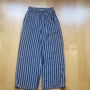 Randiga vida byxor från Bik Bok XS - Snygga blåvita randiga byxor från Bik Bok i storlek XS. Byxorna har hög midja med resår och ett loose, wide fit. Perfekta för en chill och trendig look, tillverkade i ett lätt och mjukt material som känns skönt mot huden.