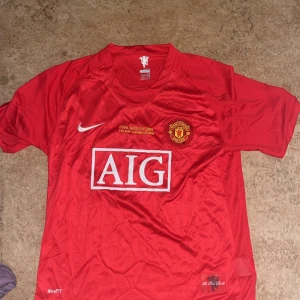 Manchester United Ronaldo 7 Finaltröja - Manchester Uniteds officiella matchtröja från Champions League-finalen 2008 i Moskva. Röd med vita detaljer, AIG-sponsor, Nike-logga och klubbmärke framtill. På ryggen står det Ronaldo och nummer 7. Tillverkad i lätt och ventilerande NikeFIT-material.