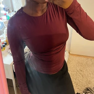 Vinröd långärmad topp med öppen rygg - Säljer en vinröd långärmad topp med tight passform och snygg öppen rygg med korsad detalj upptill. Gott som ny! 