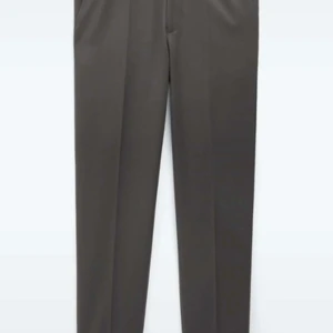 Grå kostymbyxor från Filippa K, strl 48 - Snygga grå kostymbyxor från Filippa K i storlek 48. Byxorna har rak passform, elastisk midja med snörning och diskreta bakfickor. Perfekta för en clean och stilren look. Materialet känns mjukt och följsamt.