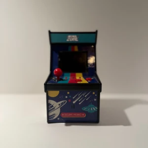 Arcade Zone - Retroinspirerad mini-arkadmaskin med färgglad rymddesign och joystick. Perfekt för dig som älskar nostalgi och klassiska spel. Liten och smidig – ta med till kompisarna eller ha på skrivbordet för en snabb spelpaus. En kul pryl för unga gamers och retrofans! Det finns 240 spel