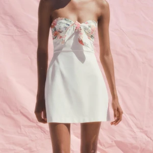 Vit kort klänning med blommig rosett - Superfin axelbandslös kort klänning i vitt med en blommig rosett upptill. Intressekoll! Storlek M men passar S, har vanligtvis xs och lite stor för mig. Prislapp sitter kvar och den är endast testad en gång! Slutsåld på Zara, pris kan diskuteras 