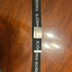 Björn Borg bälte med metallspänne - Snyggt svart bälte från Björn Borg med tydlig logga längs hela bandet. Bältet har ett robust metallspänne med ingraverad text och är gjort i slitstarkt tygmaterial. Perfekt accessoar för att lyfta din outfit med en sportig touch. Hör av vid frågor!🙌🏽 Alltid öppen till prisförslag!