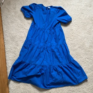 Blå långklänning från Lindex Kids - En klarblå långklänning från Lindex Kids i storlek 152. Klänningen har korta puffärmar med resår och flera volanger i kjolen för en flowy look. Tillverkad i bomull, perfekt för dig som gillar färg och enkel stil. Helt oanvänd!💓